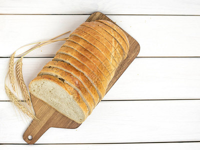 木板上的新鲜切片面包和小麦在白图片