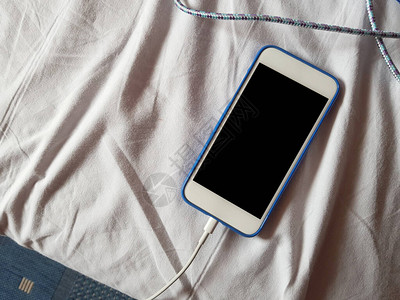 一个白色的无名电话在一张有褶皱的床单成分的凌乱床上充电图片