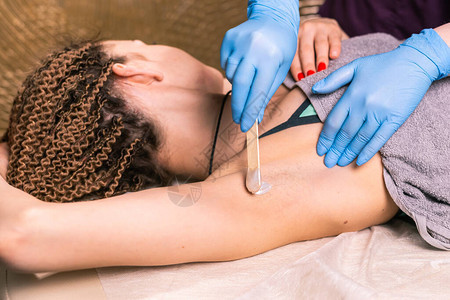 用抹刀给女人腋窝打蜡沙龙蜡美容师脱毛程序由治疗师为女身体打蜡脱毛光图片