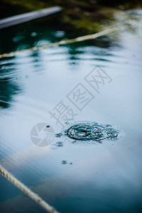 在水坑的水面上下着雨滴黑影和蓝天空的反射都是从图片