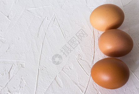 白色纹理背景上的三个棕色鸡蛋图片