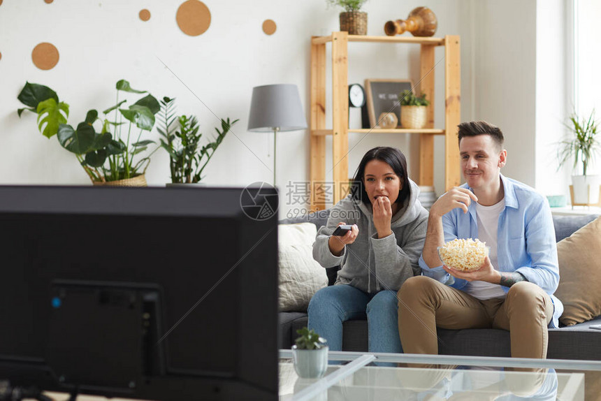 坐在沙发上吃爆米花和在家电视上看有趣的电图片