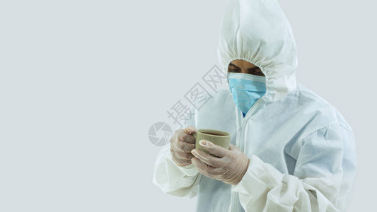 戴着蓝色面具和生物防护服的医生用手拿着一杯绿色的咖啡图片