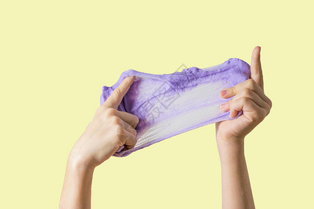 黄色背景上一个孩子的手伸出的大丁香粘液玩具抗压用于开发手部运图片