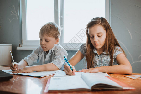 女孩和男孩在家里的抄写本上写作业图片