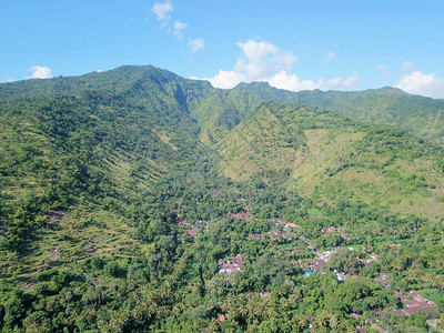 巴厘岛艾湄村上方山丘的鸟瞰图山坡上密布着热带植被和丛林山谷中的原住民房屋部分被云层覆图片