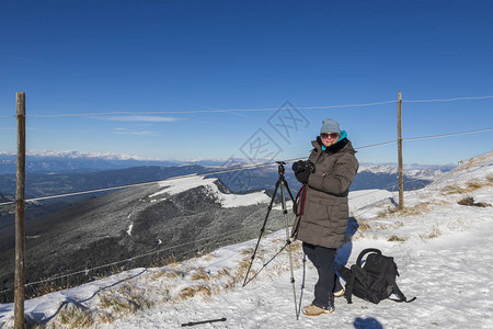 一位穿着温暖的冬季夹克和摄影装备的女人在晴朗的天气下沿着雪道走下图片
