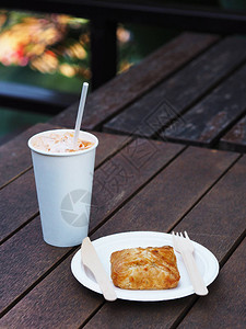 白色在户外咖啡馆的木桌上用木叉和勺子拿走一杯冷咖啡和纸盘馅饼回收和环背景图片