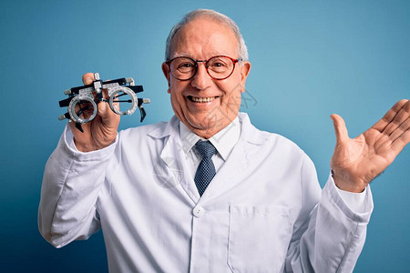 高级灰色头发长的眼科医生男子在蓝色背景上拿着观光眼镜图片