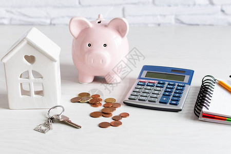 白色木制背景上的小猪硬币银行计算器和房屋模型购买房屋概念的储蓄图片