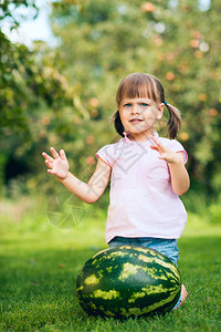 幼稚女孩在夏季花园的草坪上被大西瓜围着背景图片