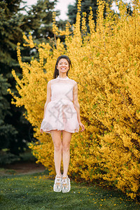 穿白裙子的年轻女子玩得很开心跳上公园露出百花的图片