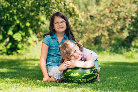 小女孩蹲在夏日花园草坪上的大西瓜旁背景图片