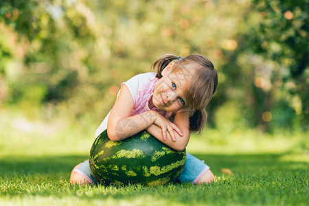 幼稚女孩在夏季花园的草坪上被大西瓜围着背景图片