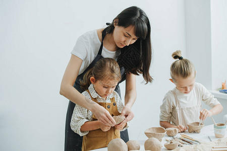 黑发妇女教孩子如何亲手在私人车间制作粘土餐具图片