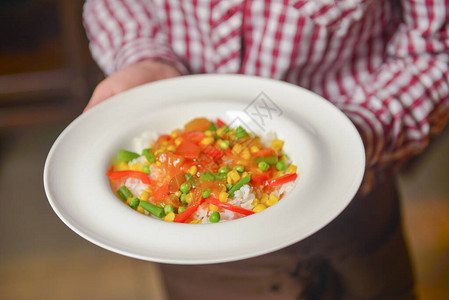 服务员用红绿黄辣椒西红柿红洋葱芹菜供应米饭美味健康素食餐的概图片