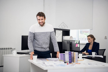 一位微笑的建筑师在他的办公室与背景中的同事的肖像图片
