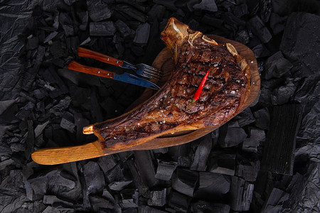木盘上的烤战斧牛排准备食用在背景煤上图片