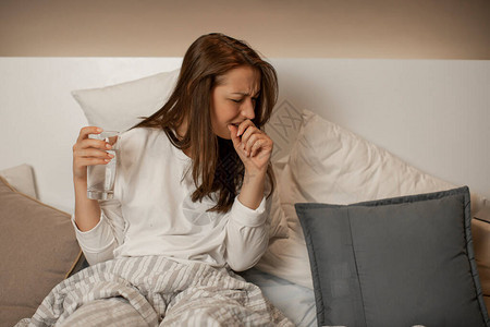 穿着便衣的漂亮女孩手握着水杯坐在床上夜深图片