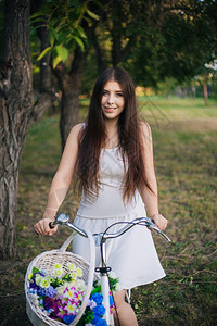 微笑的年轻女子坐在自行车上晚上在公园里背景图片