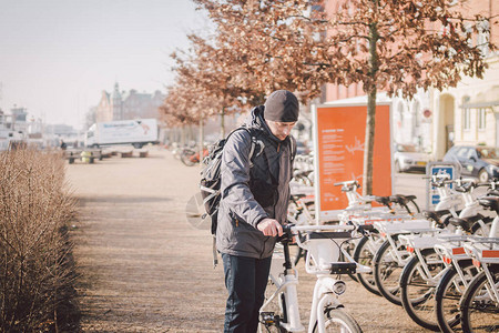 男子在哥本哈根租用白色电动自行车电动自行车出租站男停放城市自行车出租图片