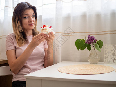 一个穿着粉红色T恤的女人坐在白桌边想对垃圾食品说不带水果的糖蛋糕图片