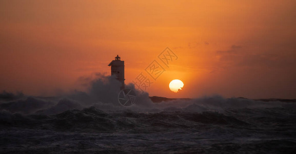 灯塔在美丽的夕阳下被薄风暴的波浪包裹着灯塔建在它得名的岩石上图片