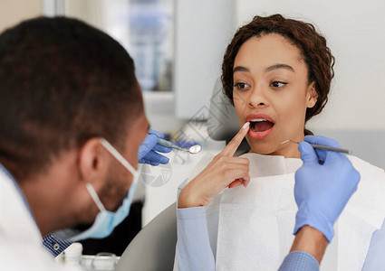 坐在牙医椅上向非洲医生展示牙齿的女病人图片
