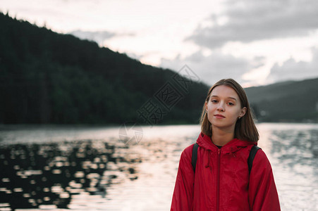 穿着红色雨衣的漂亮女孩站在山中湖的背景上图片