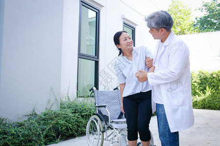 亚裔老人医生支持一名坐轮椅的女病人站立起来步行康复加强双腿图片