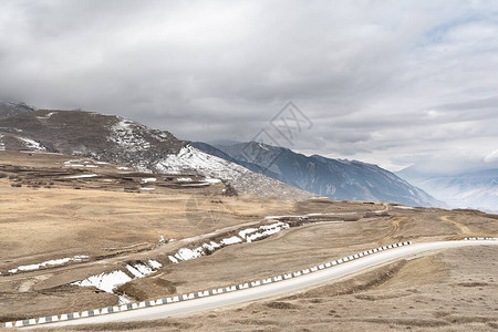 以阴沉的天空的山峰为背景的高山公路景观图片