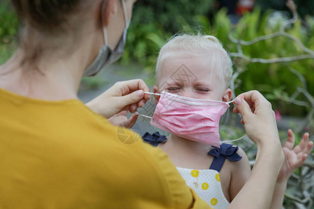 妈努力将医用口罩戴在孩子的脸上鲁莽的蹒跚学步的女孩拒绝戴防护面罩大流行科罗纳爆发期图片