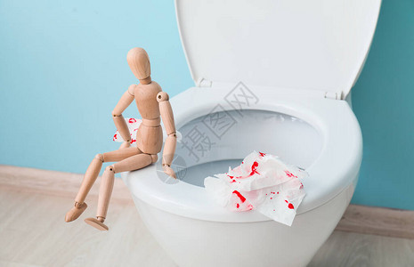 马桶木制人形和厕所里有血迹的纸痔疮概念图片