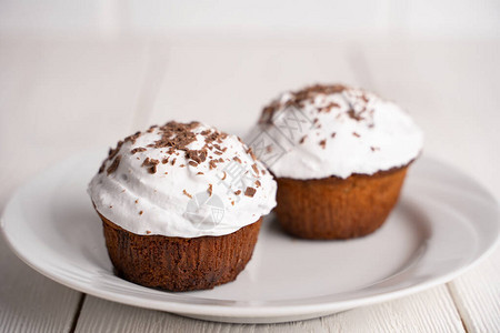 白木桌上的白色板块上加奶油和巧克力片的杯子蛋糕菜单或糖果制品目录的图片