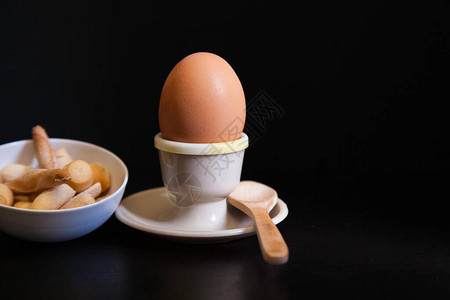 鸡蛋木勺和陶瓷碗中的软煮蛋黑底的面包图片