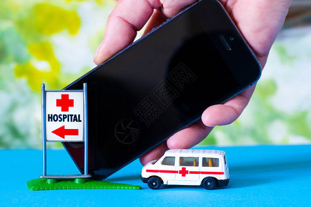 一辆玩具救护车和在标志医院附近用电话手牵着蓝色和绿图片