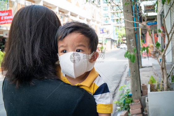 身着N95面罩的亚洲可爱男孩和母亲在户外城市建筑中保护Corona和空气污图片