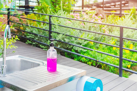 花园铝水槽上的粉色酒精凝胶瓶或抗菌肥皂消毒剂图片