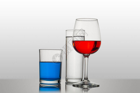 白色背景的杯子和水晶杯以及不同类型和颜色的饮料图片