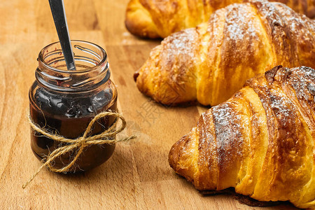 新鲜的烤羊角面包和果酱在木质桌子上的罐子里加了莓果酱法国早餐概图片