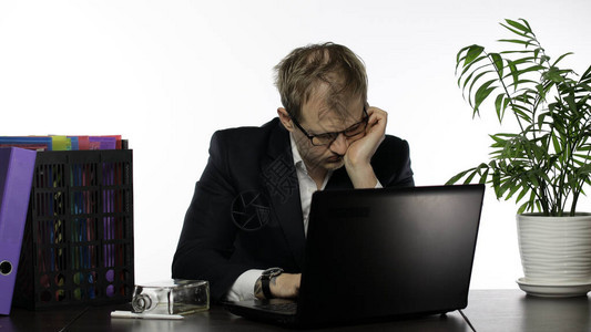 疲惫的邋遢的职员坐在办公桌前的笔记本电脑上努力工作桌上的酒精干邑情绪西装衬衫眼镜的男商人白色背景图片