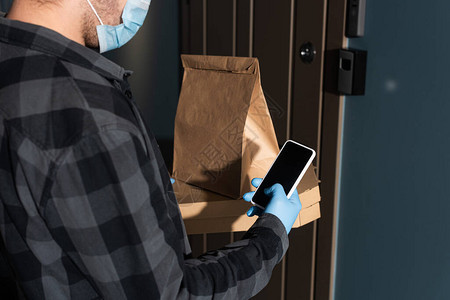 入口处门附近的医用口罩包裹比萨盒和智能手机中的图片
