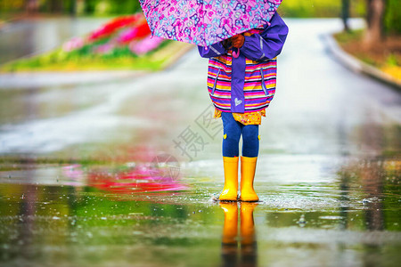 带着雨伞和橡皮靴的快乐女孩在春日散图片