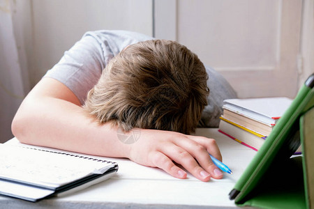 疲倦的男孩躺在桌子上学习和考试的概念pc平板电脑和教科书的男孩睡着了对家庭作业的背景图片