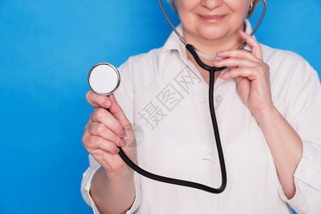 穿白色大衣在蓝色背景上使用听诊器的老天主教医生女图片