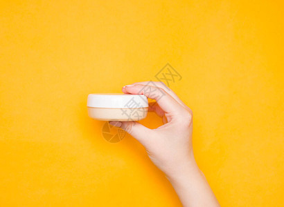 女人用奶油手放在透明罐子里白盖子在黄色的明亮背景图片