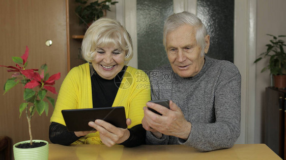快乐的老成熟退休夫妇拿着智能手机和平板电脑看着手机屏幕图片
