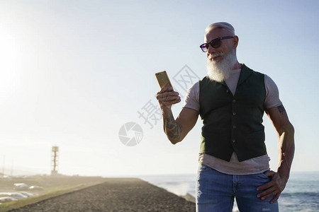 时尚老人在海边使用智能手机应用程序图片