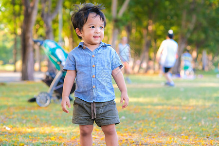 穿着蓝色衬衫的快乐小男孩站在城市公园的绿草场上微笑着蹒图片