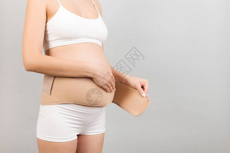 年轻孕妇穿着内衣的裁剪图像在她的腹部贴上妊娠绷带图片
